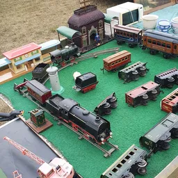 Uitgestalde verzameling miniatuurtreinen en wagons op groen speelbord met stations en accessoires