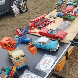 Verzameling speelgoedauto's en voertuigen uitgestald op een tafel, waaronder een rode brandweerwagen, blauwe kraan, turquoise