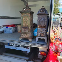 Twee antieke kachels met decoratieve details op het laadplatform van een bestelwagen