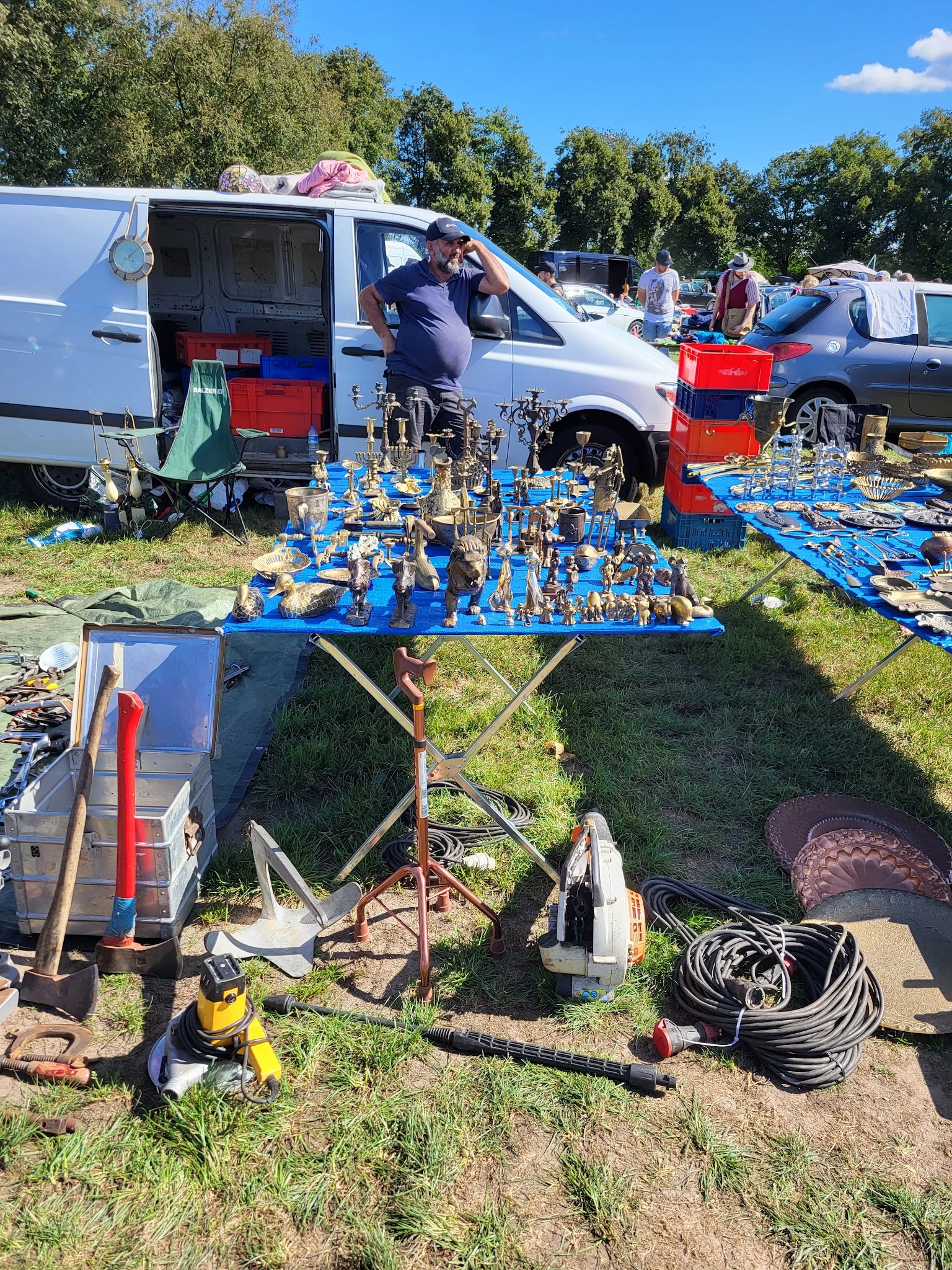 Blauwe marktafel met veel gouden beeldjes en figuren op een carbootsale met vans en kramen op de achtergrond
