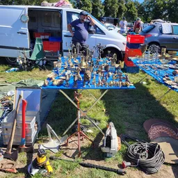 Blauwe marktafel met veel gouden beeldjes en figuren op een carbootsale met vans en kramen op de achtergrond