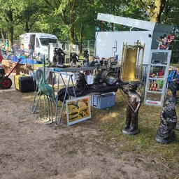 Kraampje op carbootsale met diverse gebruiksartikelen, beelden en meubels uitgestald op en rond een tafel