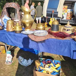 Uitgestalde tweedehands items op een blauwe tafel, waaronder koperen kannen, borden en decoratieve objecten