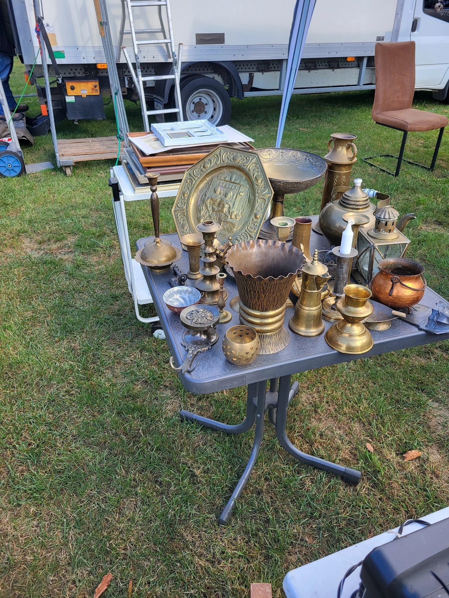 Uitgestalde antieke en vintage messingwerk, kandelaars, schalen en decoratieve objecten op een tafel buiten
