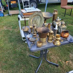 Uitgestalde antieke en vintage messingwerk, kandelaars, schalen en decoratieve objecten op een tafel buiten