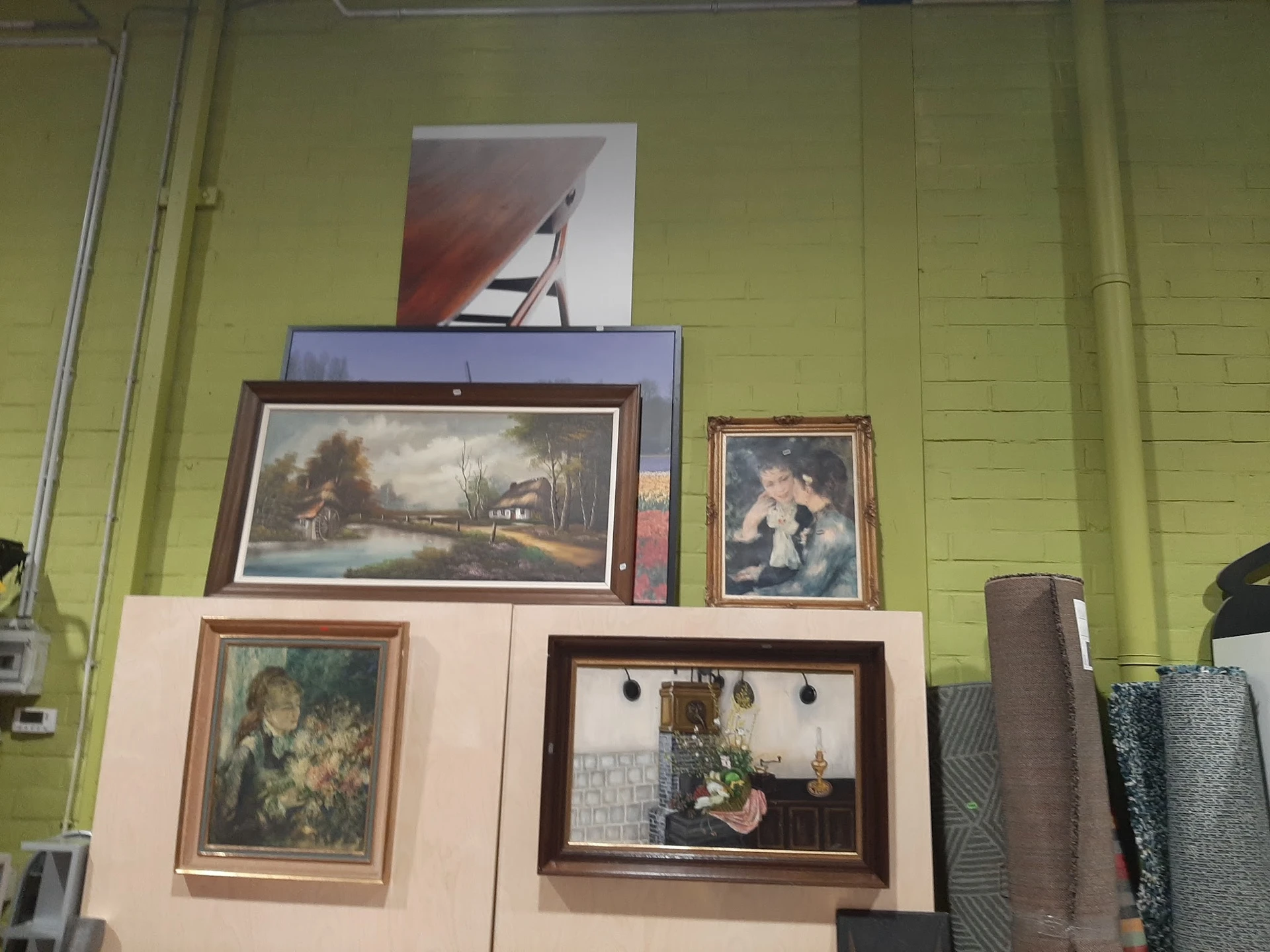 Uitgestalde schilderijen en kunstwerken in verschillende formaten en framesoorten tegen gele wand