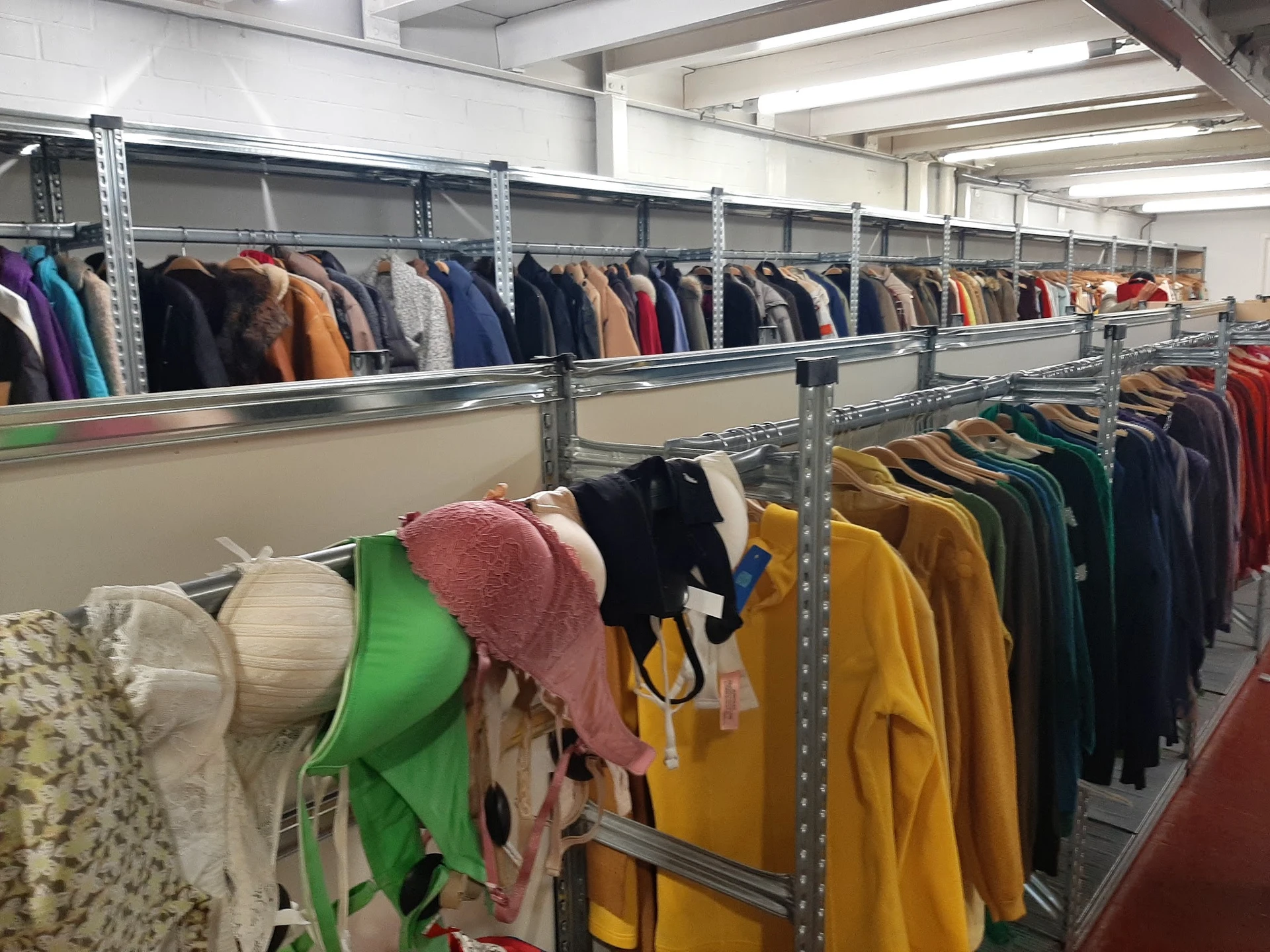 Metalen stellingen met uiteenlopende tweedehands kleding in verschillende kleuren en stijlen