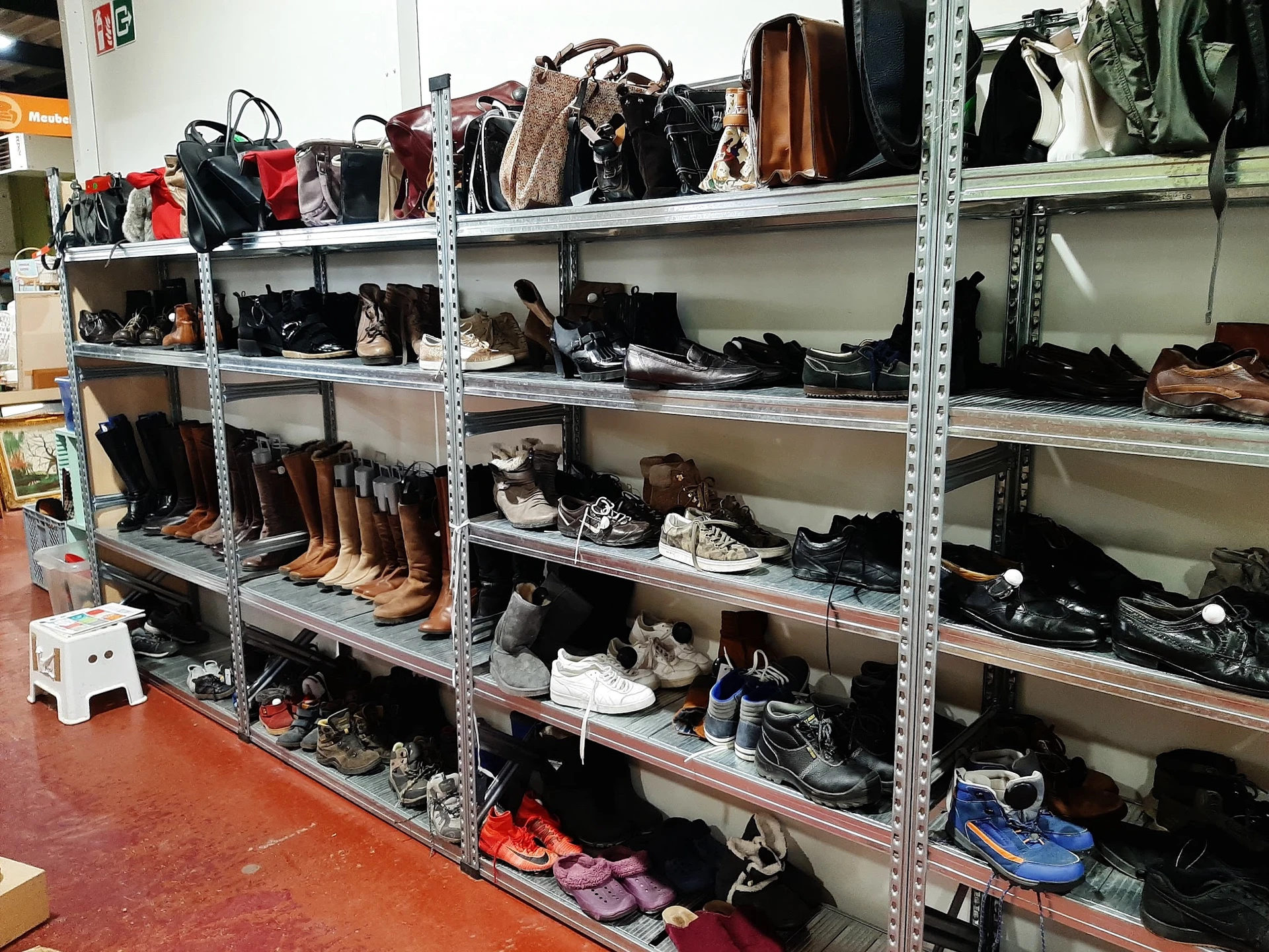 Metalen stellingen gevuld met tweedehands tassen, schoenen en accessoires in een kringloopwinkel