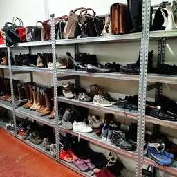 Metalen stellingen gevuld met tweedehands tassen, schoenen en accessoires in een kringloopwinkel
