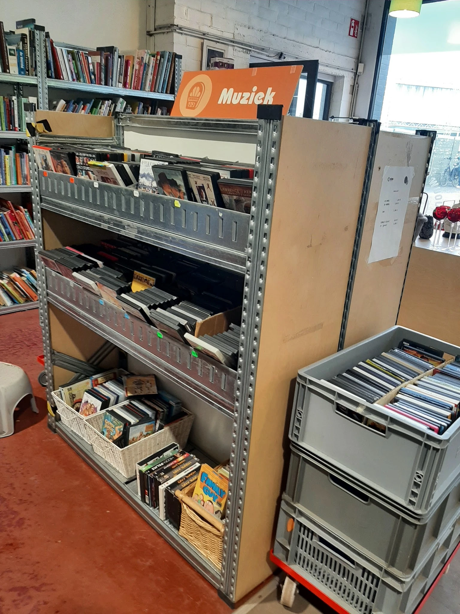 Metalen stellingen met cd's, dvd's en boeken, waaronder zwarte kisten met schijven op de onderste plank