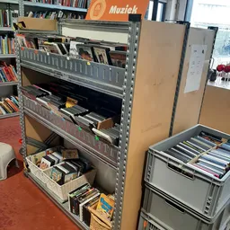 Metalen stellingen met cd's, dvd's en boeken, waaronder zwarte kisten met schijven op de onderste plank