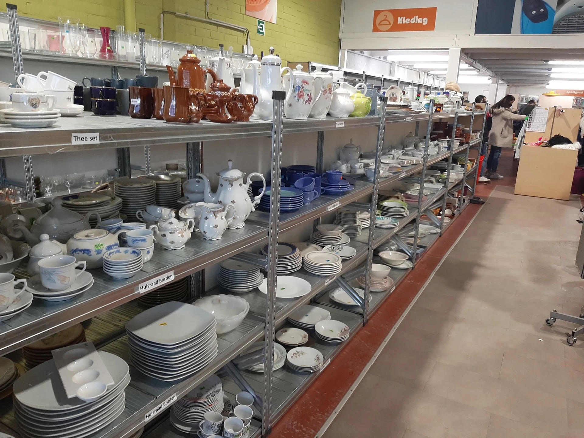 Stellingen met serviesgoed, borden, kopjes en aardewerk in verschillende kleuren en stijlen