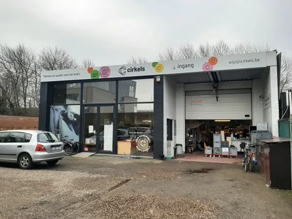 Voorkant van kringloopwinkel Cirkels met witte gevel, grote ramen en ingang, parkeerplaats met auto ervoor