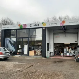 Voorkant van kringloopwinkel Cirkels met witte gevel, grote ramen en ingang, parkeerplaats met auto ervoor