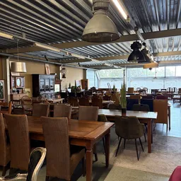 Ruime winkelvloer met houten tafels, stoelen en diverse meubels uitgestald onder industriële hanglamp