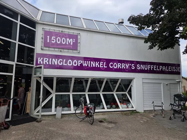 Voorgevel van kringloopwinkel met paars uithangbord en grote raampartijen, fiets ervoor geparkeerd