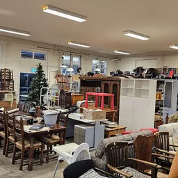 Ruim interieur van kringloopwinkel met tafels, stoelen, kasten en diverse meubels uitgestald