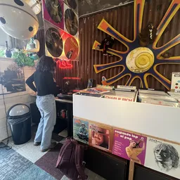 Winkelinterieur met vinyl platen op de voorgrond, neonreclames en decoratieve schijven aan de muur, klant aan het kijken