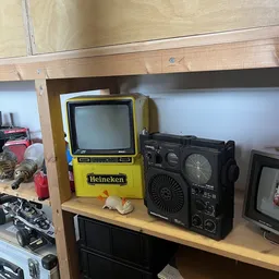 Stellingkast met vintage elektronica: gele Heineken-tv, zwarte boombox en andere retro-apparaten