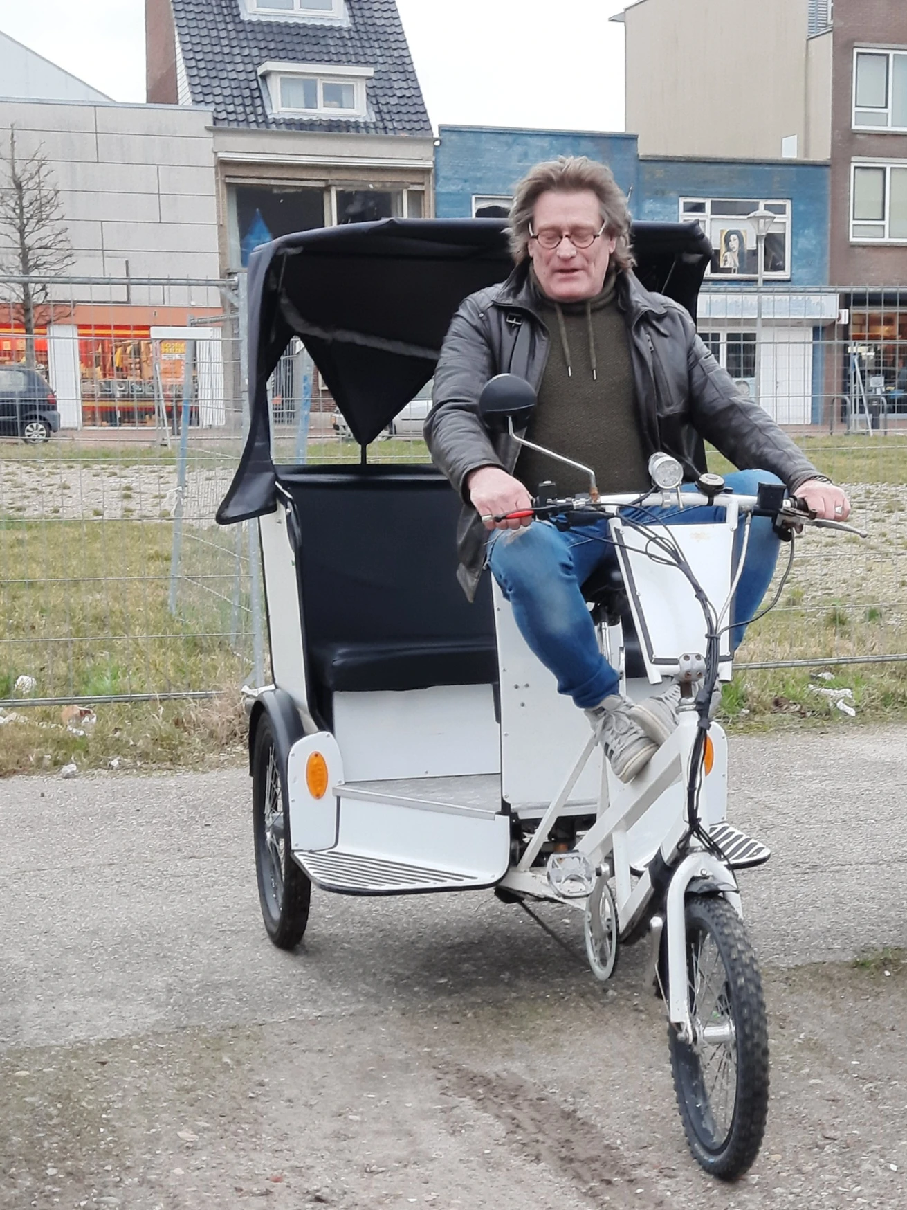 Man op driewielige bakfiets met zwart zonnescherm op parkeerterrein