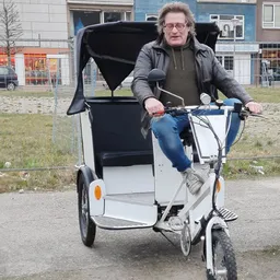 Man op driewielige bakfiets met zwart zonnescherm op parkeerterrein