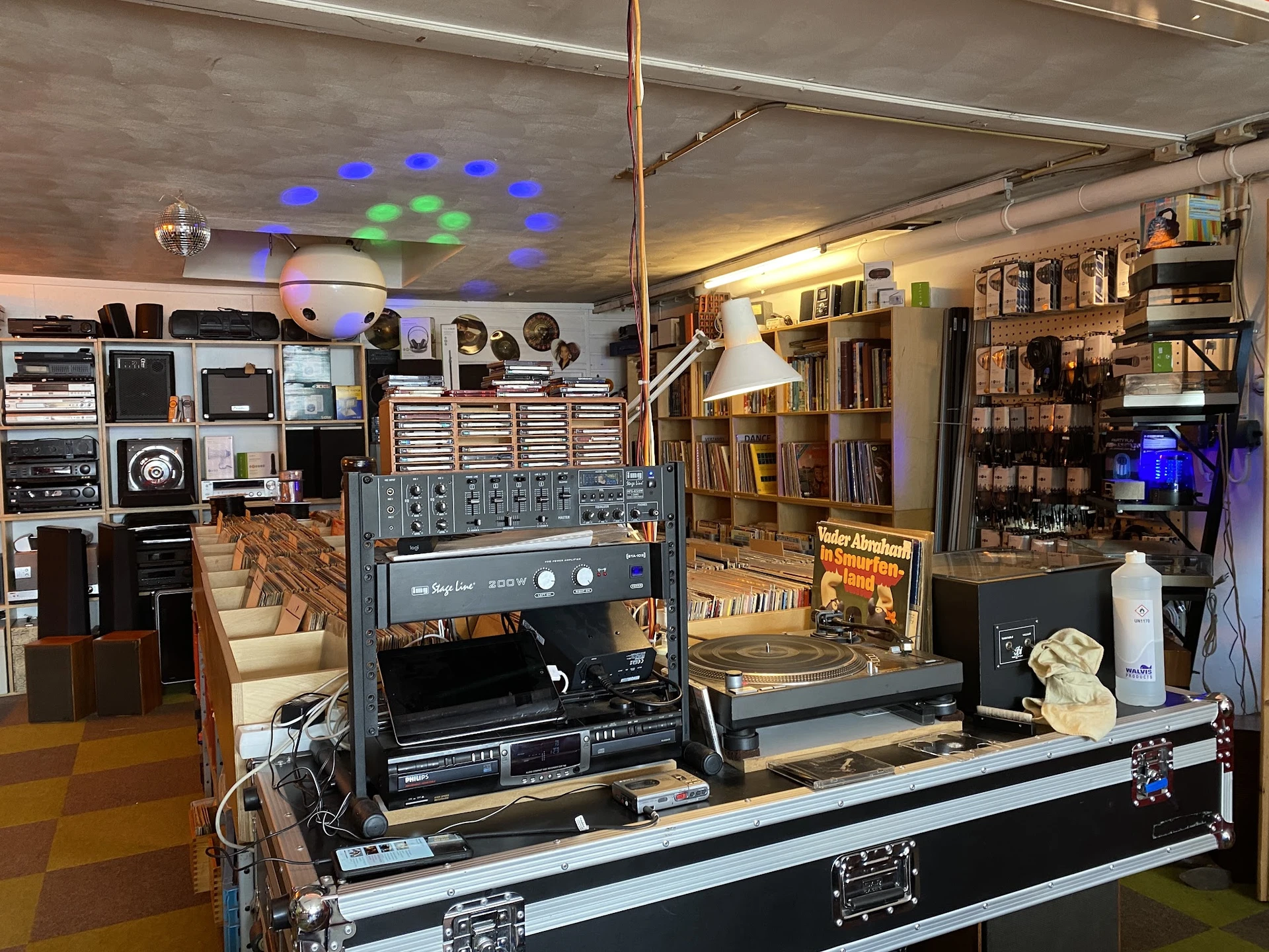 Winkelbinnenkant met vintage audio-apparatuur, versterkers, platen en boeken op stellingen, blauwe verlichting aan plafond