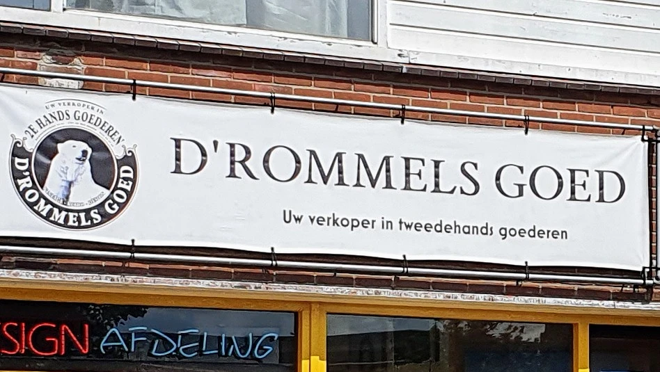Winkelpui met wit reclamebord 'D'ROMMELS GOI' en Nederlands ondertekst, gele deur met 'AFDELING' in neonblauw