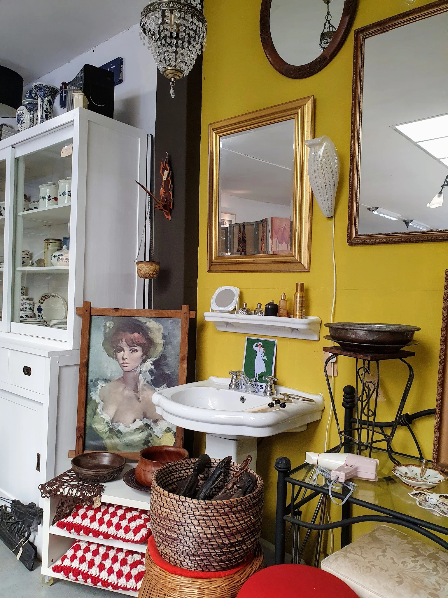 Winkelbinnenkant met gele muur, vintage wastafel, spiegel, portretschilderij en diverse antieke spullen
