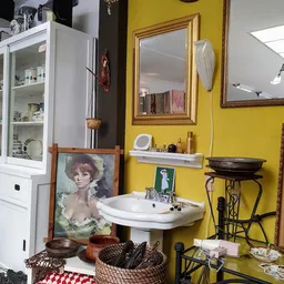 Winkelbinnenkant met gele muur, vintage wastafel, spiegel, portretschilderij en diverse antieke spullen