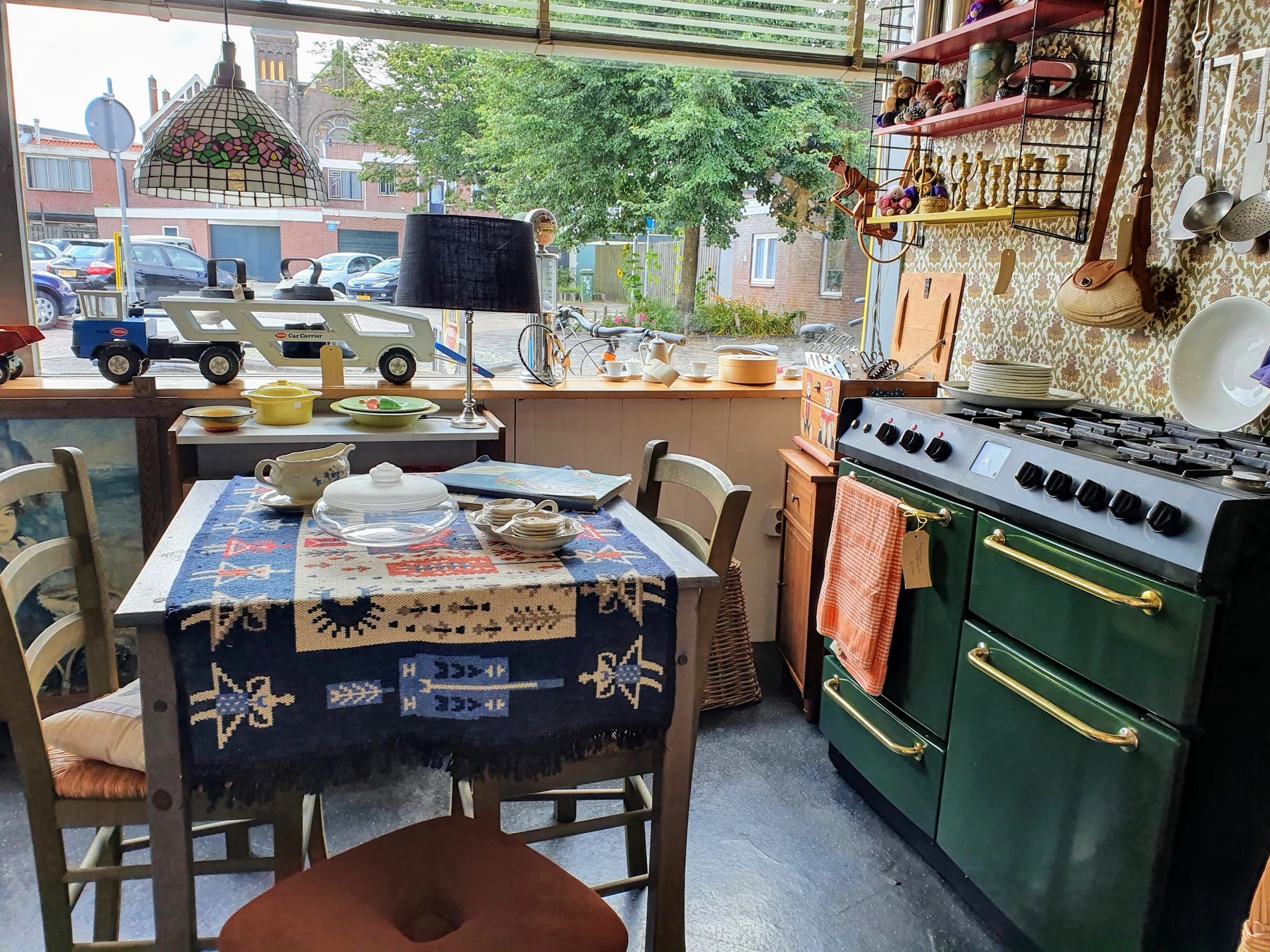 Vintage winkelbinnenruimte met tafel met kleed, stoelen, groene retro-oven en houten stellingen met antieke spullen