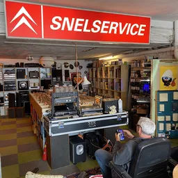 Winkelvloer met stellingen vol vintage apparaten, elektronica en spullen; man aan flipperkasten