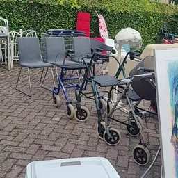 Diverse tweedehands artikelen op een terras: rollatoren, stoelen, tassen en een schilderij