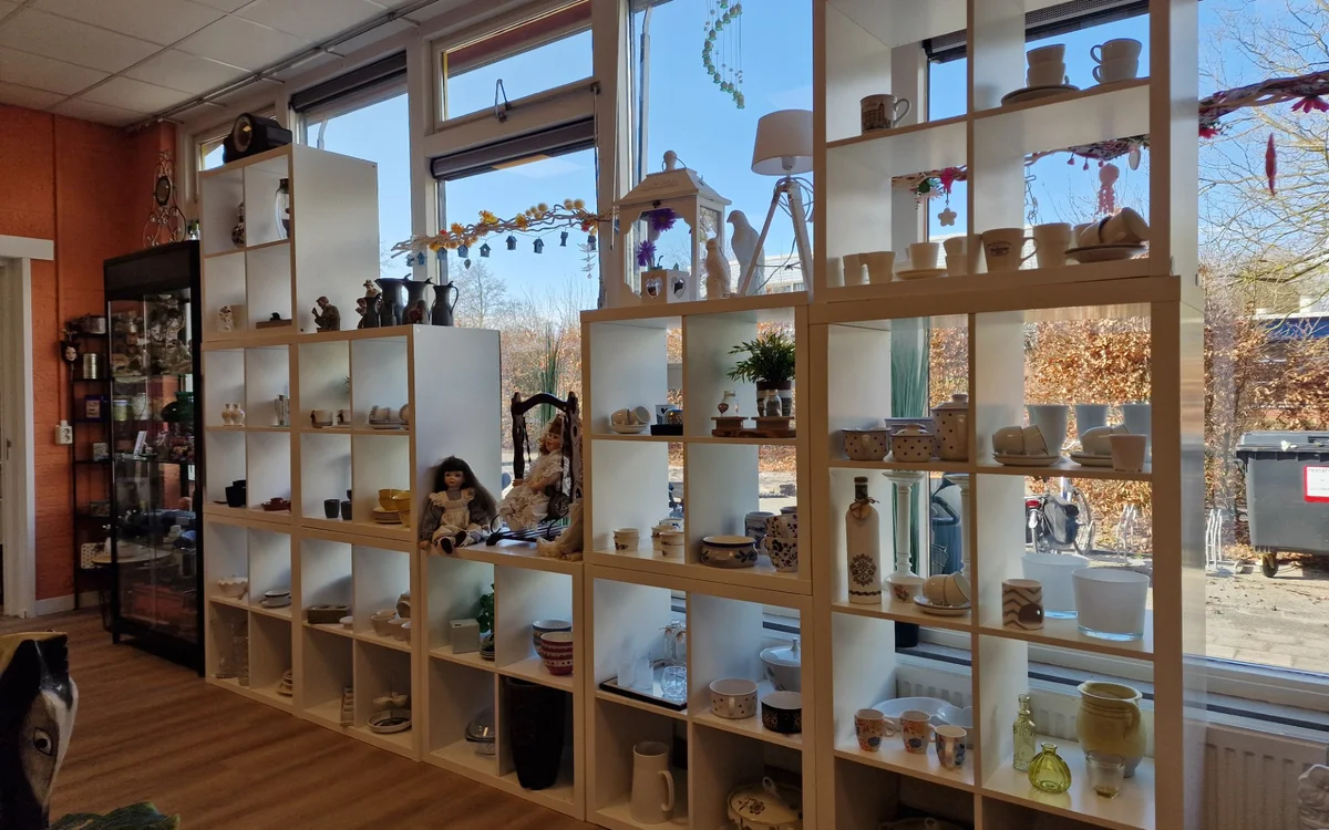 Houten stellingsysteem met vakken gevuld met diverse huishoudartikelen, servies en decorstukken in kringloopwinkel