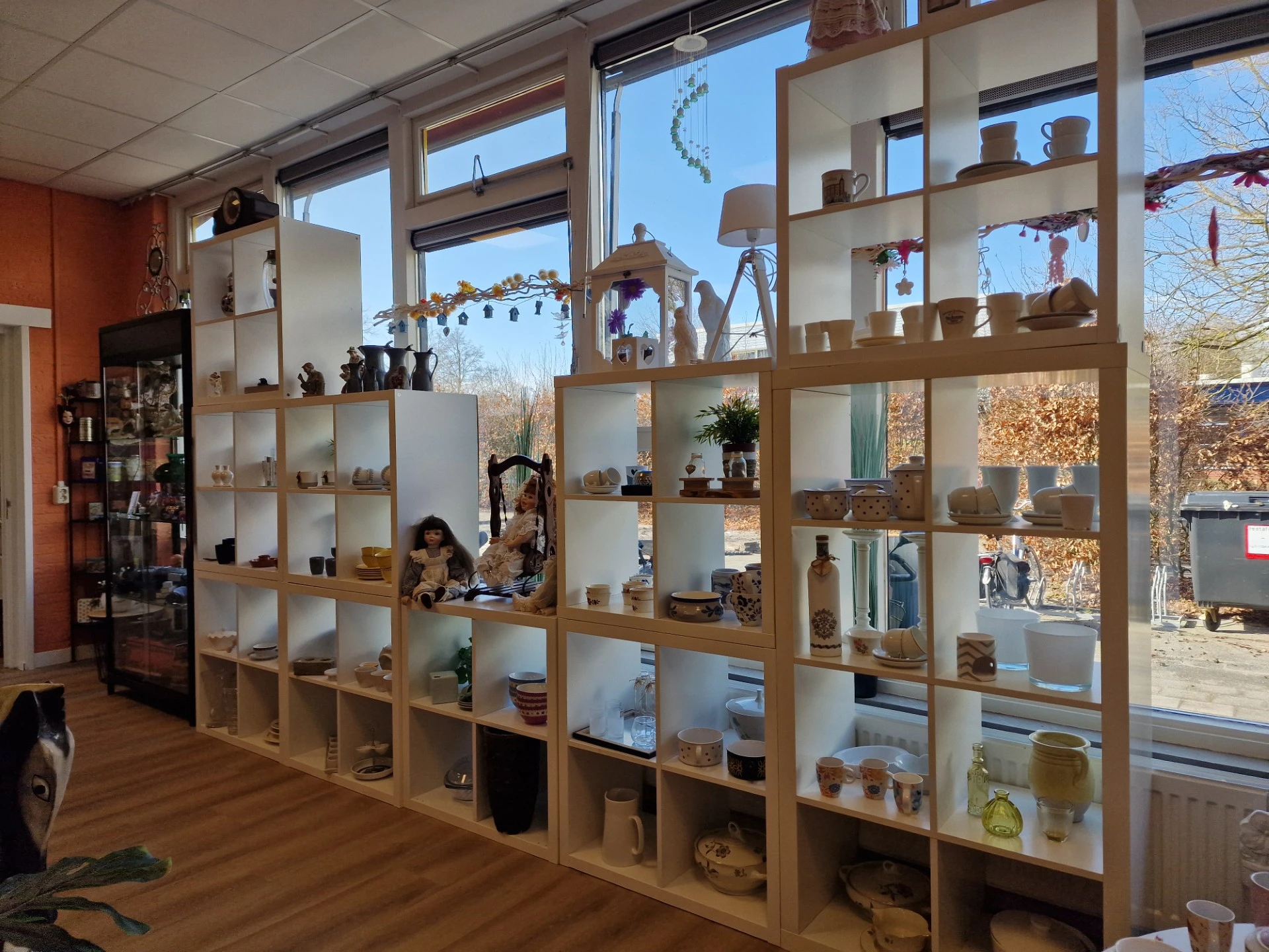 Houten stellingsysteem met vakken gevuld met diverse huishoudartikelen, servies en decorstukken in kringloopwinkel