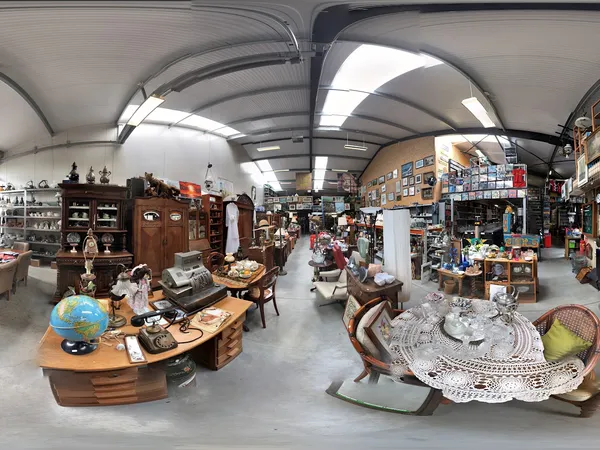 Ruim interieur van kringloopwinkel met diverse meubels, huishoudartikelen en spullen uitgestald onder verlichte plafondpanele