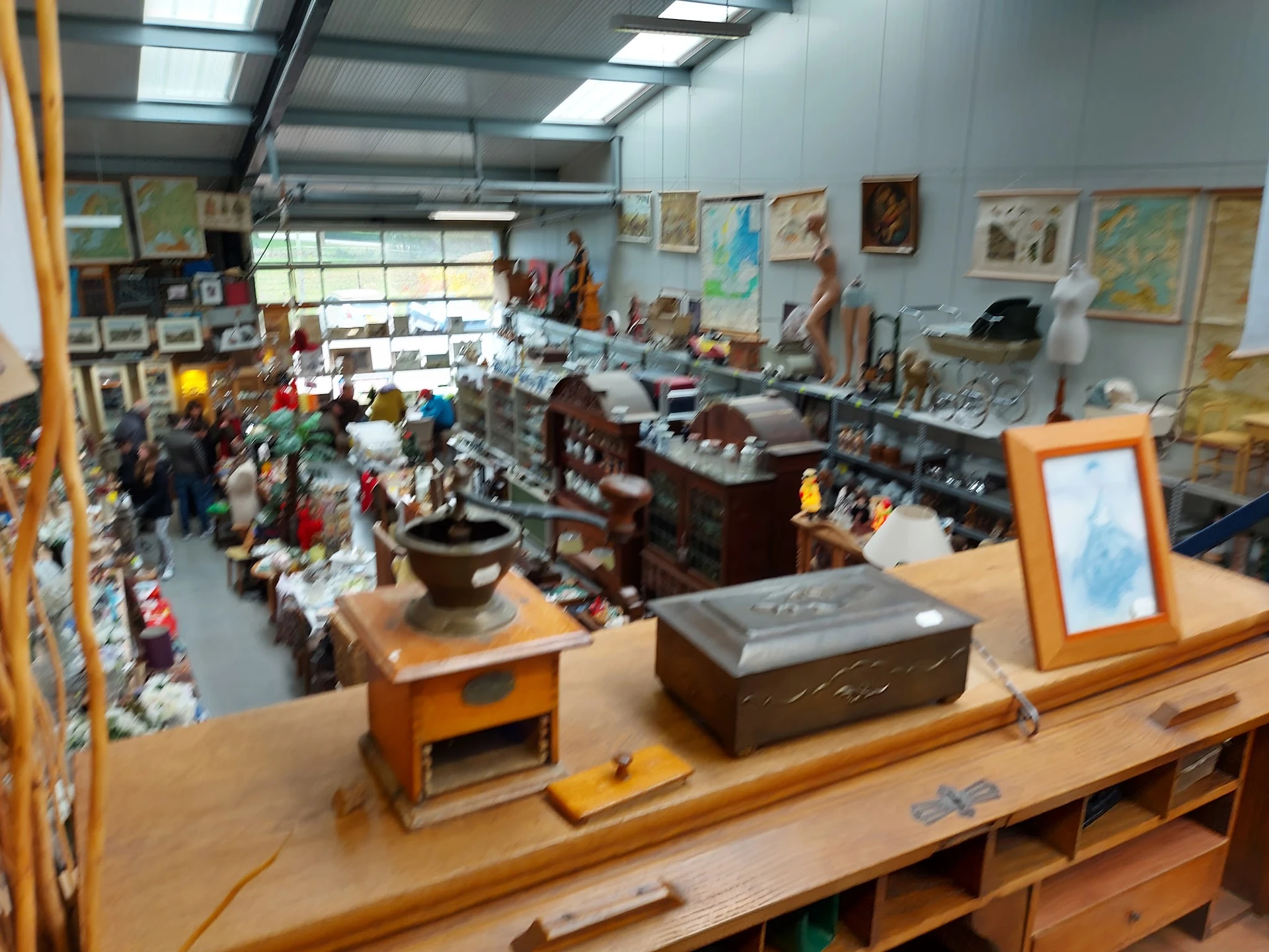 Overzicht van kringloopwinkelinterieur met diverse meubels, kunstwerken aan muren en bezoekers op de vloer