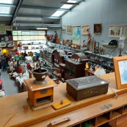 Overzicht van kringloopwinkelinterieur met diverse meubels, kunstwerken aan muren en bezoekers op de vloer