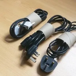 Drie elektrische snoeren met stekkers en witte labels, op houten ondergrond