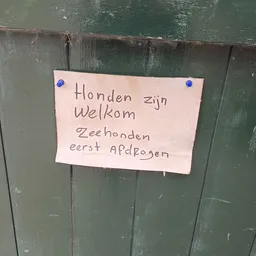 Handgeschreven briefje op groene deur met Nederlandse tekst