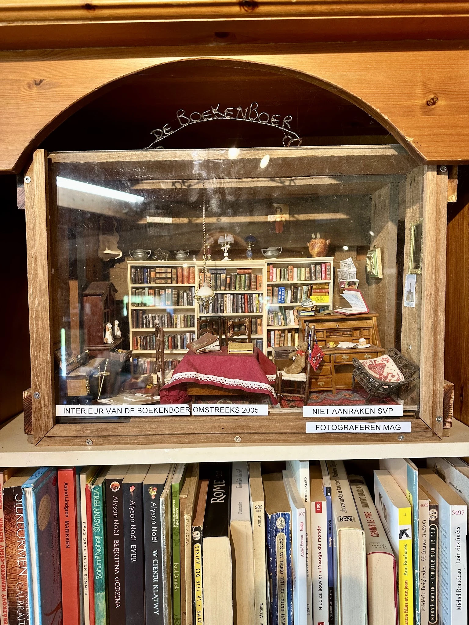 Miniatuurdiorama van een huiskamer met boekenkasten, bed en meubels in een vitrinekast