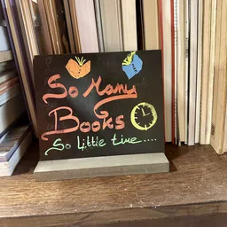 Bord met handgeschreven tekst 'So Many Books So little time' met getekende boeken en klok