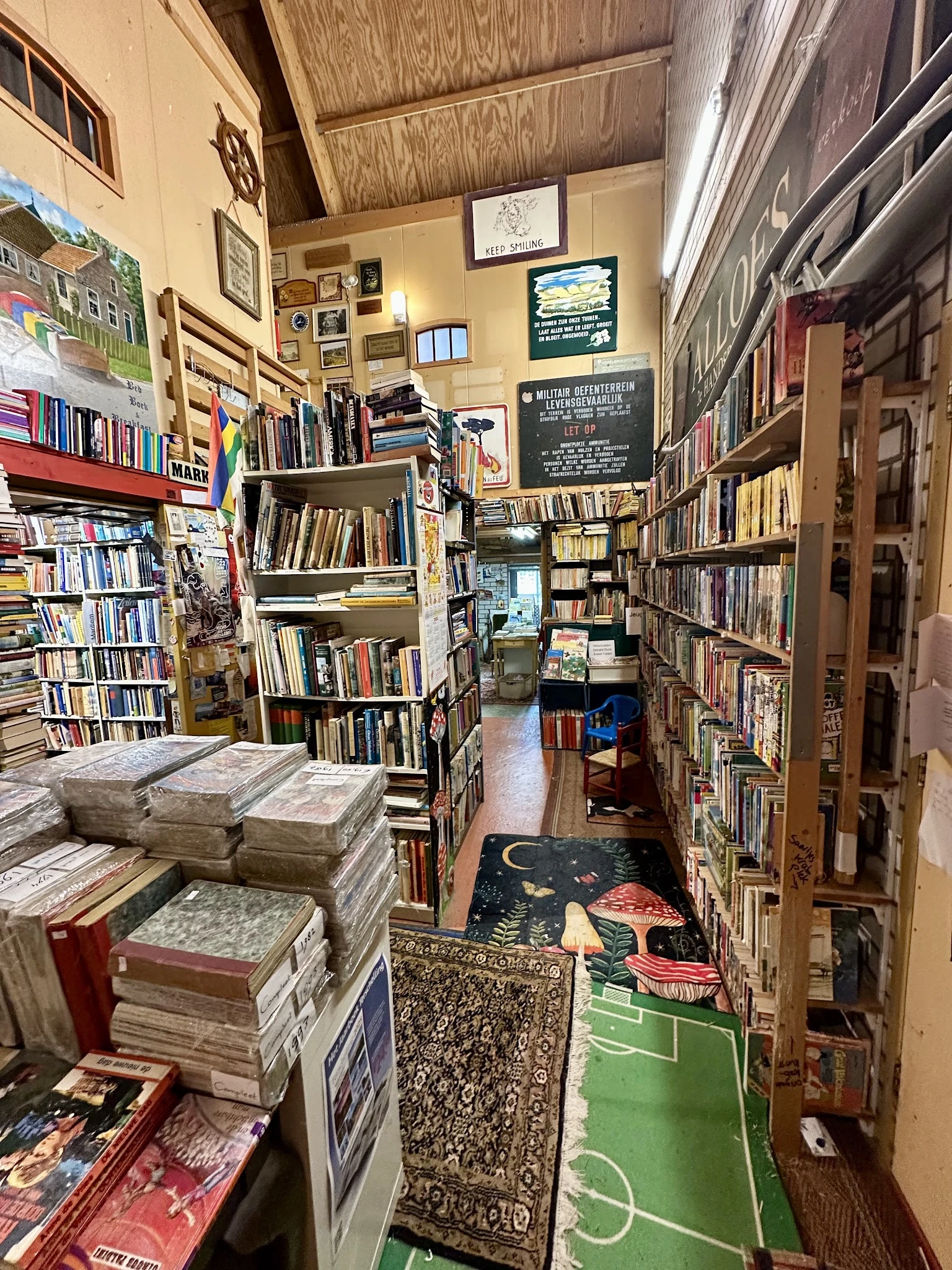 Smalle winkelgang vol boekenrekken en stapels boeken, met decoratie op de vloer