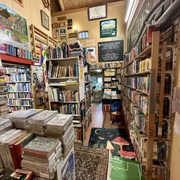 Smalle winkelgang vol boekenrekken en stapels boeken, met decoratie op de vloer