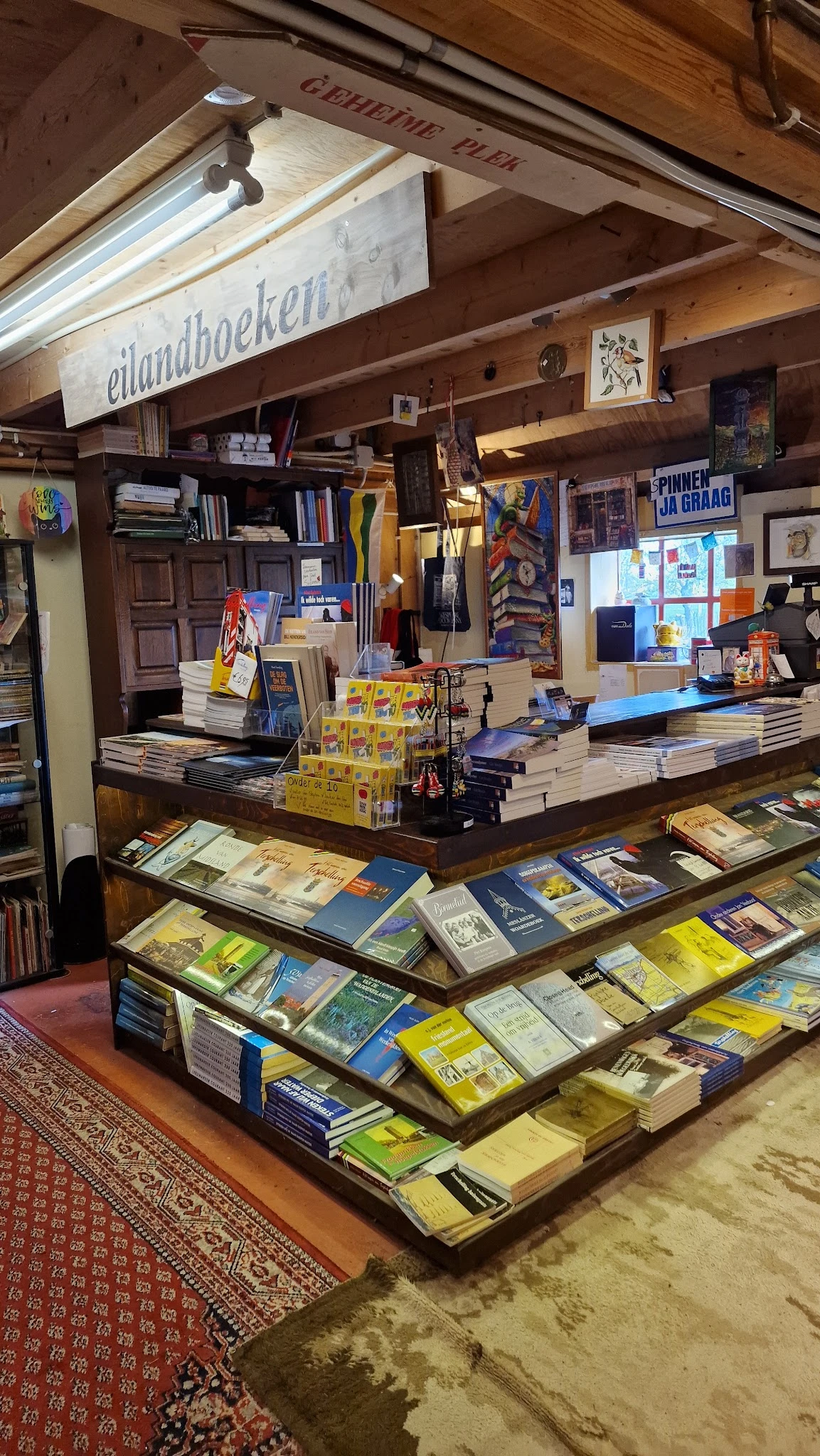 Boekenwinkel interieur met toonbank, boeken op stellingen en in vitrines, gele dozen en diverse artikelen.