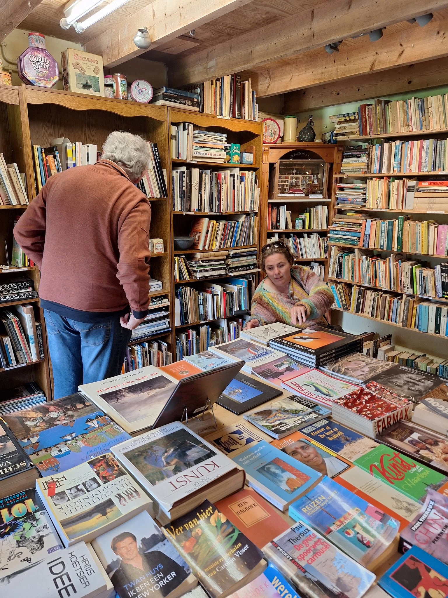 Boekenwinkel met bezoekers die tussen boekenkasten bladeren; op tafel liggen uitgelegde boeken en andere artikelen
