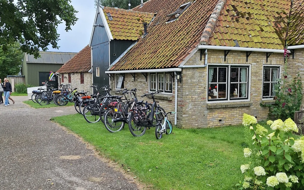 Voorkant van stenen kringloopwinkel met gele dakpannen, fietsen geparkeerd op het gazon, groene hortensia's op de voorgrond