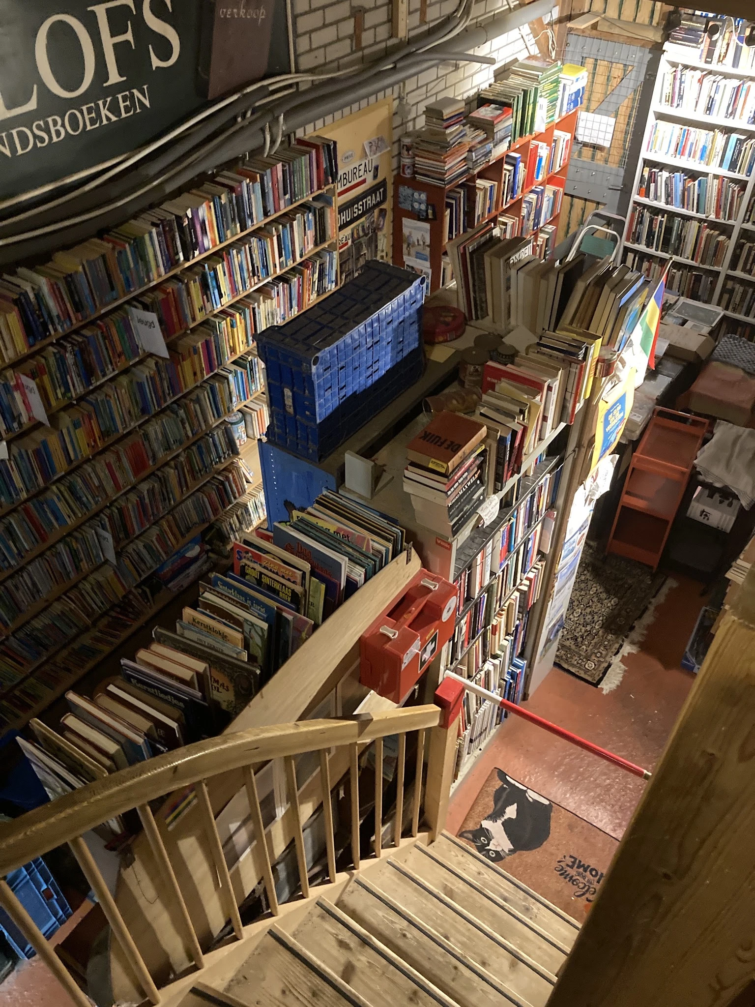 Overzicht van boekenwinkel met volle stellingen en dozen met boeken op meerdere niveaus