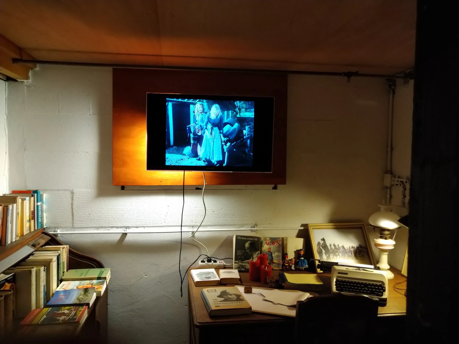 Werkkamer met televisie, bureau, boekenkasten en diverse spullen op de muur