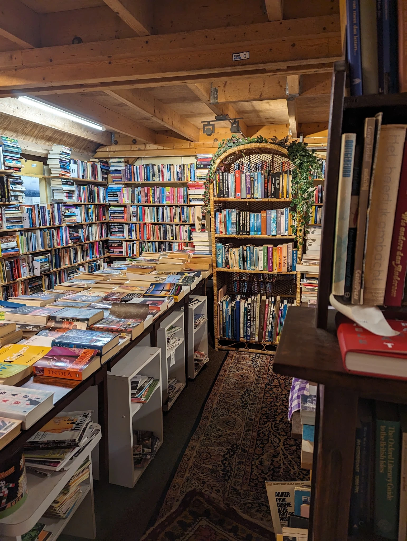 Binnenruimte van boekenwinkel met boekenkasten tegen de wanden, boeken op tafels en sterke houten constructie zichtbaar