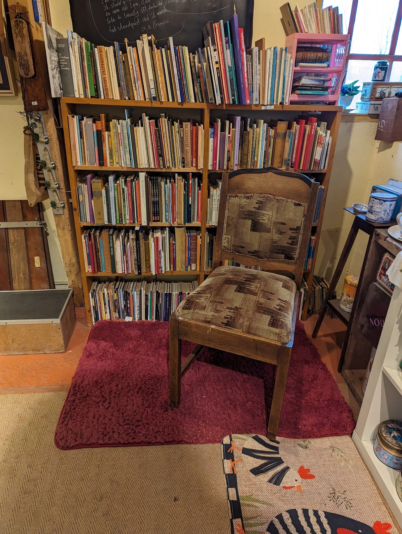Houten stoel op wijnrode vloermat voor boekenkasten vol cd's en dvd's
